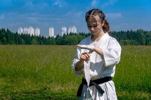 Teenager Mädchen im ein Kimono Verpackung ein Handgelenk wickeln um ihr Hand Vor nehmen Karate draußen foto