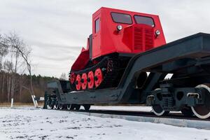 Schlepper auf ein Eisenbahn Flachwagen gegen das Hintergrund von ein Wald im Winter foto