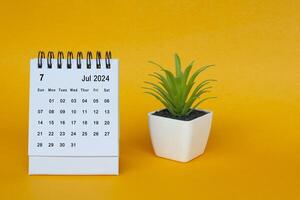 Juli 2024 Schreibtisch Kalender mit eingetopft Pflanze auf Gelb Hintergrund. foto