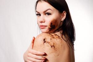 Brünette Frau reinigt das Haut von das Körper Kaffee schrubben foto