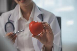 Hände von Arzt Frau halten rot Herz, zeigen Symbol von Liebe, Mensch Unterstützung zu geduldig, fördern medizinisch Versicherung, früh Untersuchung zum Gesundheitspflege, Kardiologe Hilfe. schließen oben von Objekt foto