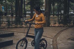 glücklich jung asiatisch Frau während Reiten ein Fahrrad im ein Stadt Park. sie lächelte mit das Fahrrad von Transport. ökologisch freundlich Konzept. foto