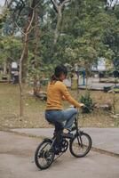 glücklich jung asiatisch Frau während Reiten ein Fahrrad im ein Stadt Park. sie lächelte mit das Fahrrad von Transport. ökologisch freundlich Konzept. foto