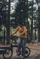 glücklich jung asiatisch Frau während Reiten ein Fahrrad im ein Stadt Park. sie lächelte mit das Fahrrad von Transport. ökologisch freundlich Konzept. foto