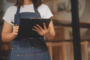 Startup erfolgreicher Kleinunternehmer SME Schönheitsmädchen steht mit Tablet-Smartphone im Café-Restaurant. Porträt der Barista-Café-Besitzerin mit asiatischer Bräune. KMU-Unternehmer-Verkäufer-Geschäftskonzept foto