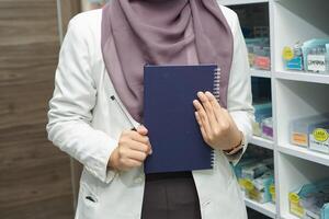 schließen oben Hand bringen Buch von Muslim Frauen Apotheker tragen Hijab im Krankenhaus foto