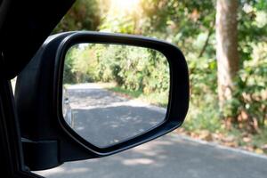 Rückseite Aussicht Spiegel von Auto auf Asphalt Straße Hintergrund. Kopieren Raum und verschwommen von Grün Wald beim Tag Zeit. foto