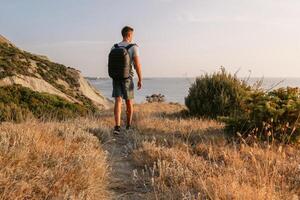 Wanderer Mann mit Rucksack Wandern auf das Ozean Küste mit Berge und Abend Sonnenlicht. foto