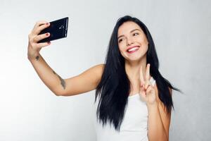 Selfie Zeit. jung lächelnd blond haarig Dame tun Selfie auf grau Hintergrund foto