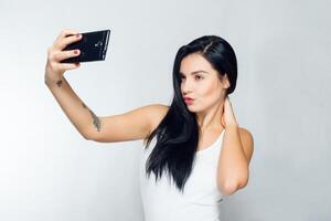 Selfie Zeit. jung lächelnd blond haarig Dame tun Selfie auf grau Hintergrund foto