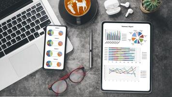 ein organisiert Schreibtisch mit ein Laptop, Smartphone, Tablette zeigen bunt Kuchen Diagramme, ein Stift, Gläser, Kaffee, und Kopfhörer, symbolisieren ein Fachmann Geschäft Analyse Arbeitsplatz. foto