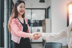 zwei Fachmann Frauen mit hell lächelt einnehmend im ein Handschlag im ein modern Büro, symbolisieren ein erfolgreich Geschäft Zustimmung oder Partnerschaft. foto