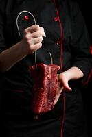 ein Metzger hält ein Stück von Kalbfleisch auf ein Metall Haken. Fleisch Vorbereitung. auf ein schwarz Hintergrund. foto