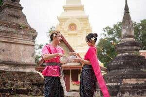 jung thailändisch Paar tragen thailändisch Kostüme spielen im das Wasser während Songkran im das Tempel foto