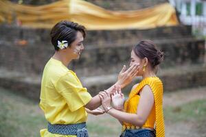 ein schön jung thailändisch Paar tragen thailändisch Kostüme spielen im das Wasser während Songkran im das Tempel foto