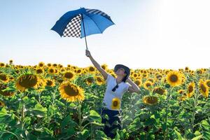 Frau mit Hut im ein Sonnenblume Feld mit Regenschirm foto