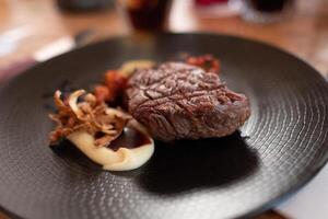 Rindfleisch Filet mit rustikal püriert Kartoffeln, geröstet Kirschen und Confit Knoblauch Soße auf dunkel Teller foto