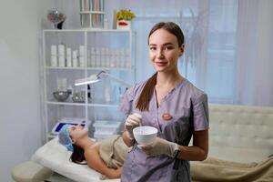 glücklich weiblich Kosmetikerin bereitet vor das Arzneimittel. Porträt ziemlich Frau tragen Weiß Handschuhe und Uniform. Schönheit, Kosmetologie Konzept. foto