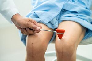 asiatisch Arzt verwenden Hammer klopfen Senior Frau geduldig zu prüfen Knie Reflex, Nerv und Muskel im Krankenhaus. foto