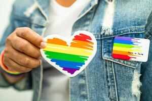 asiatische dame, die regenbogenflaggenarmbänder trägt und rotes herz hält, symbol des lgbt-stolzmonats, feiert jährlich im juni sozial für schwule, lesbische, bisexuelle, transgender, menschenrechte. foto