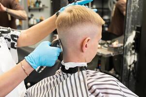 ein Junge ist Sitzung im ein Barbier Geschäft, Schneiden seine Haar mit ein Clipper foto