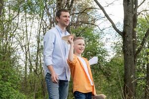 Papa Spaziergänge mit seine Sohn mit ein Papier Flugzeug draußen im das Park. foto