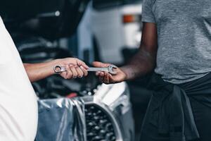 Mechanik Hand senden ein Schlüssel Werkzeug zu ein Freund. Automobil Garage Arbeiter Zusammenarbeit Reparatur Bedienung Konzept. foto