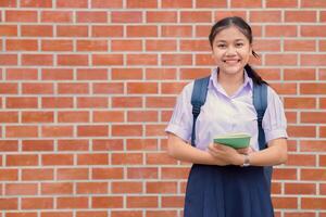 thailändisch asiatisch Schule Mädchen Teen glücklich Lächeln im Uniform Griff Buch und Schule Tasche mit Kopieren Raum foto