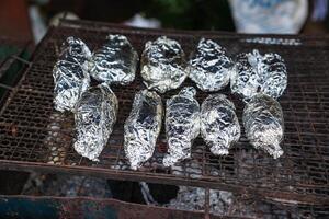 Fisch oder Kartoffel eingewickelt Abdeckung mit Aluminium vereiteln Papier Grillen auf Holzkohle Herd foto