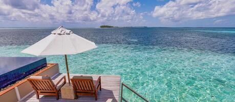 Luxus Strand Erholungsort, Bungalow in der Nähe von endlos Schwimmbad Über schön Blau Meer. tolle tropisch Insel, Sommer- Ferien Konzept. Paar Stühle mit Regenschirm, perfekt Sommer- Freizeit Ferien Urlaub Panorama foto