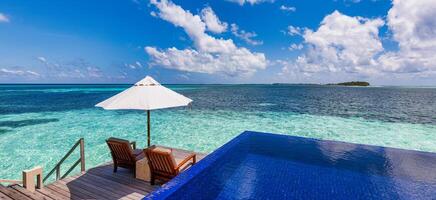 Luxus Strand Erholungsort, Bungalow in der Nähe von endlos Schwimmbad Über schön Blau Meer. tolle tropisch Insel, Sommer- Ferien Konzept. Paar Stühle mit Regenschirm, perfekt Sommer- Freizeit Ferien Urlaub Panorama foto