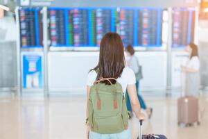 jung Frau mit Tasche und Gepäck suchen zu Flug Zeit Information Tafel im International Flughafen, Vor prüfen In. reisen, Urlaub, Ausflug und Transport Konzept foto