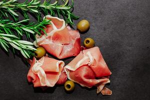 Stücke von getrocknet Schweinefleisch Jamon Prosciutto mit Oliven auf ein schwarz Tafel. foto