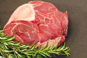 frisch Stück von Fleisch groß Rindfleisch Steak auf das Knochen Markknochen mit ein Zweig von Rosmarin auf ein schwarz Hintergrund. foto