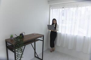 ein japanisch Frau Überprüfung Smartphone durch Fernbedienung Arbeit im das Zuhause Büro foto