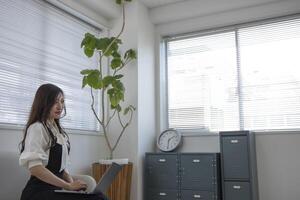 ein japanisch Frau Überprüfung Smartphone durch Fernbedienung Arbeit im das Zuhause Büro foto