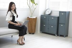 ein japanisch Frau Überprüfung Smartphone durch Fernbedienung Arbeit im das Zuhause Büro foto