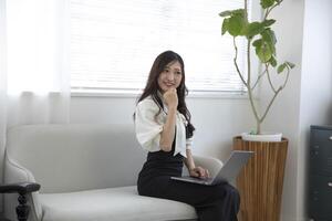 ein japanisch Frau Überprüfung Smartphone durch Fernbedienung Arbeit im das Zuhause Büro foto