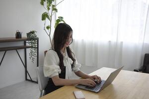 ein japanisch Frau Überprüfung Smartphone durch Fernbedienung Arbeit im das Zuhause Büro foto