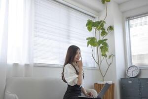 ein japanisch Frau Überprüfung Smartphone durch Fernbedienung Arbeit im das Zuhause Büro foto