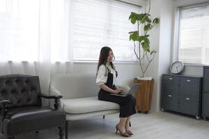 ein japanisch Frau Überprüfung Smartphone durch Fernbedienung Arbeit im das Zuhause Büro foto