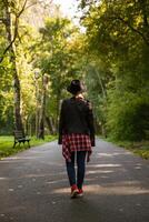 jung kaukasisch Mädchen Reisen im ein Hut und Jacke Spaziergänge das Wald oder Park im das Schatten von Bäume. verschwommen Hintergrund. hoch Qualität Foto