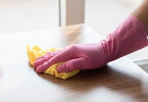 ein Hand im ein Rosa Handschuh Tücher das Oberfläche von ein hölzern Tabelle mit Gelb Mikrofaser. hoch Qualität Foto