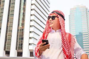 jung arabisch Geschäftsmann Stehen mit Handy, Mobiltelefon Smartphone verschwommen Stadt Hintergrund foto