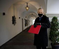 ein grau haarig Mann im ein schwarz Mantel hält ein rot Mappe im seine Hände und Uhren das Uhr. das Konzept von warten und treffen. hoch Qualität Foto