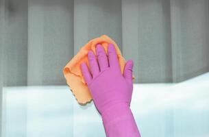 ein Hand im ein Rosa Handschuh wäscht ein Fenster mit ein Gelb Stoff auf ein sonnig Tag. hoch Qualität Foto