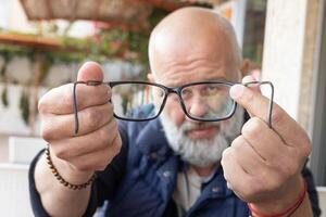 Nahansicht Porträt von ein gut aussehend Erwachsene Mann mit ein grau Bart sieht aus in Brille. Foto von Brille mit Brille und Rahmen im Fokus. hoch Qualität Foto