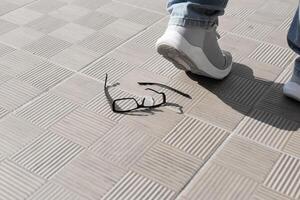 Fuß im ein grau Sneaker trat auf das Brille. gebrochen Glas auf Straße Fliesen . hoch Qualität Foto