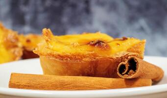 Teller mit einer Portugiesisch Pastell- de nata Kuchen mit Pudding und Zimt Stöcke. Pastell- de belem ist ein ikonisch becherförmig Gebäck mit ein verbrannt oben und ein knusprig Puff Gebäck Kruste. Süss Nachtisch. foto