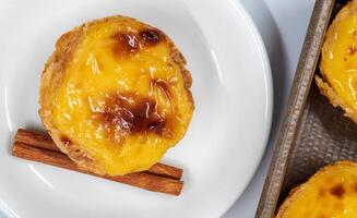 Pastell- de nata Gebäck oder Portugiesisch Ei Torte und Zimt Stöcke isoliert auf Weiß Hintergrund. Pastell- de belem ist ein klein Kuchen mit ein knusprig Puff Gebäck Kruste und ein Pudding Sahne Füllung. foto